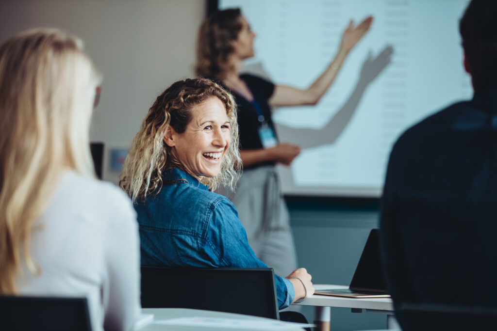 Vrouw kijkt naar achter en lacht terwijl een presentatie bezig is